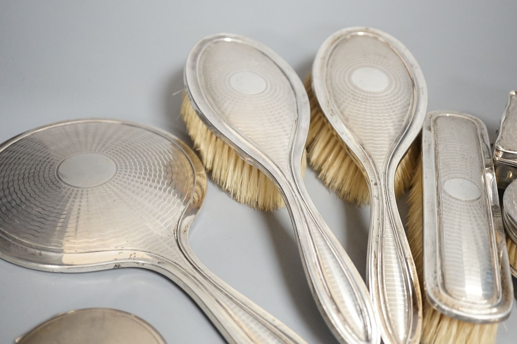 A George V engine turned silver seven piece dressing table set, comprising, two trinket boxes and a mirror, brush and comb set, Synyer & Beddoes, Birmingham, and Chester, 1912,13,14 and a silver mounted compact.